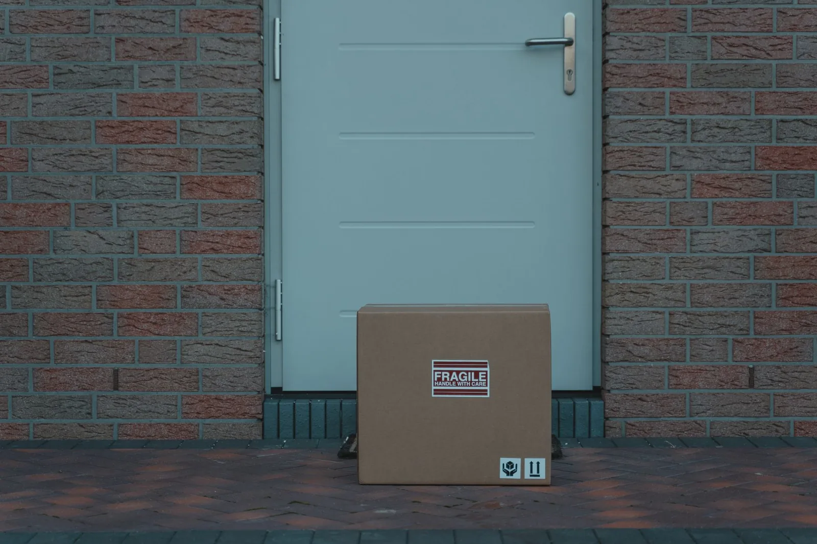 Cardboard box with a fragile sticker left at a grey door in a brick wall